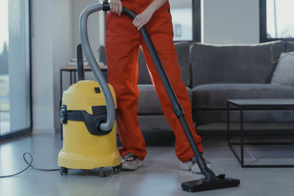 A person in coveralls standing beside a yellow vacuum